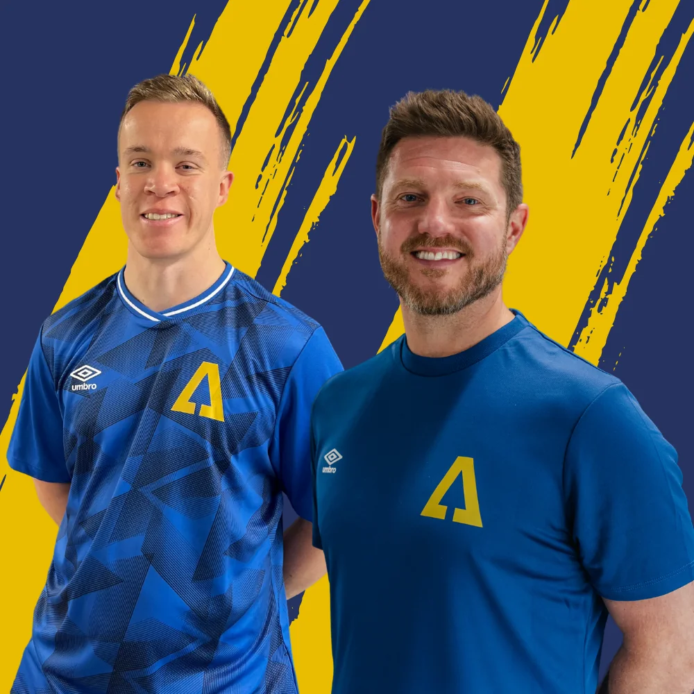 Oli Lowe and Dave Hunt smiling in blue Ascension tops in front of a navy and gold backdrop