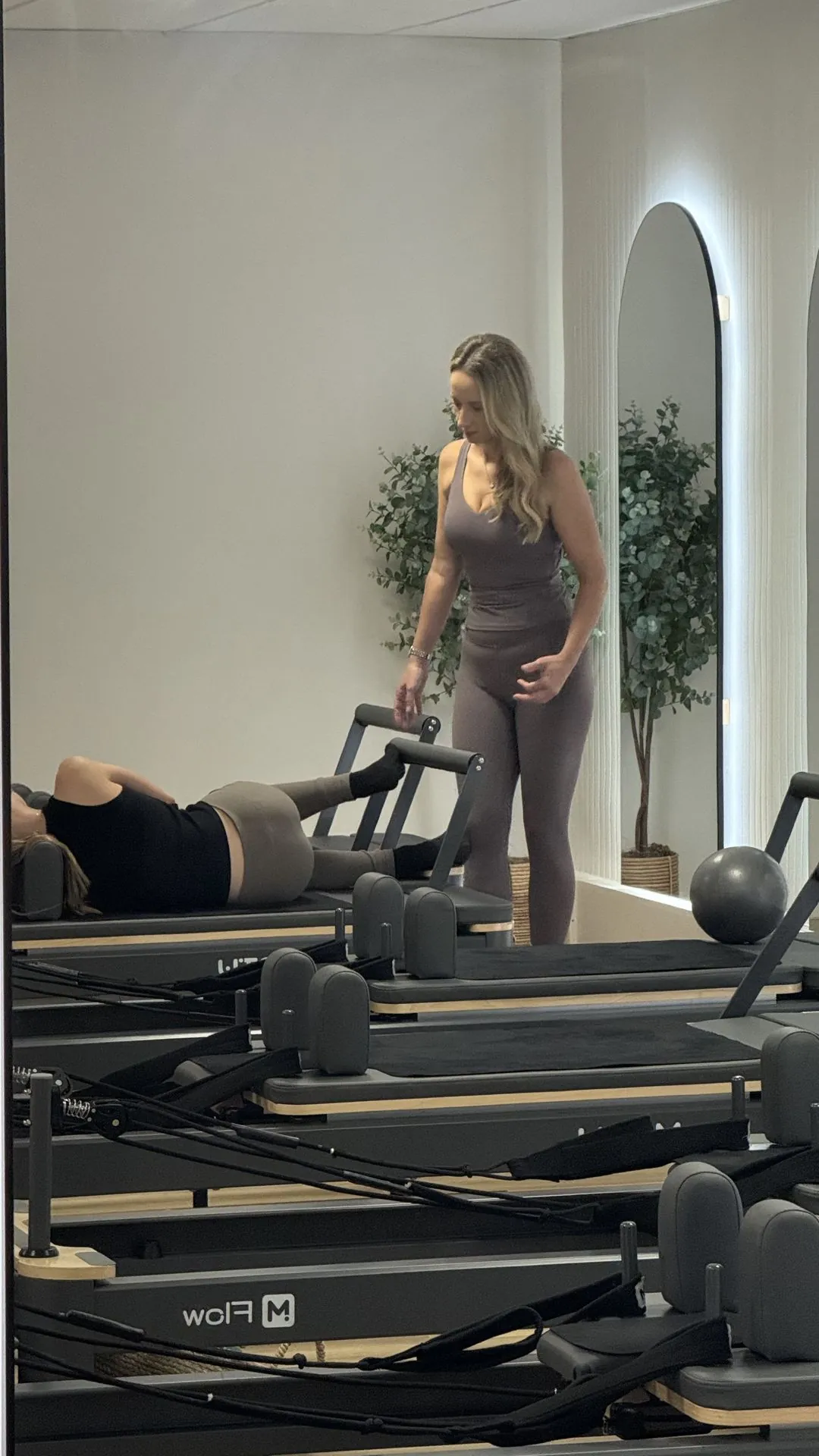 Instructor guiding a client on a reformer during a class at Ascension Reformer Pilates