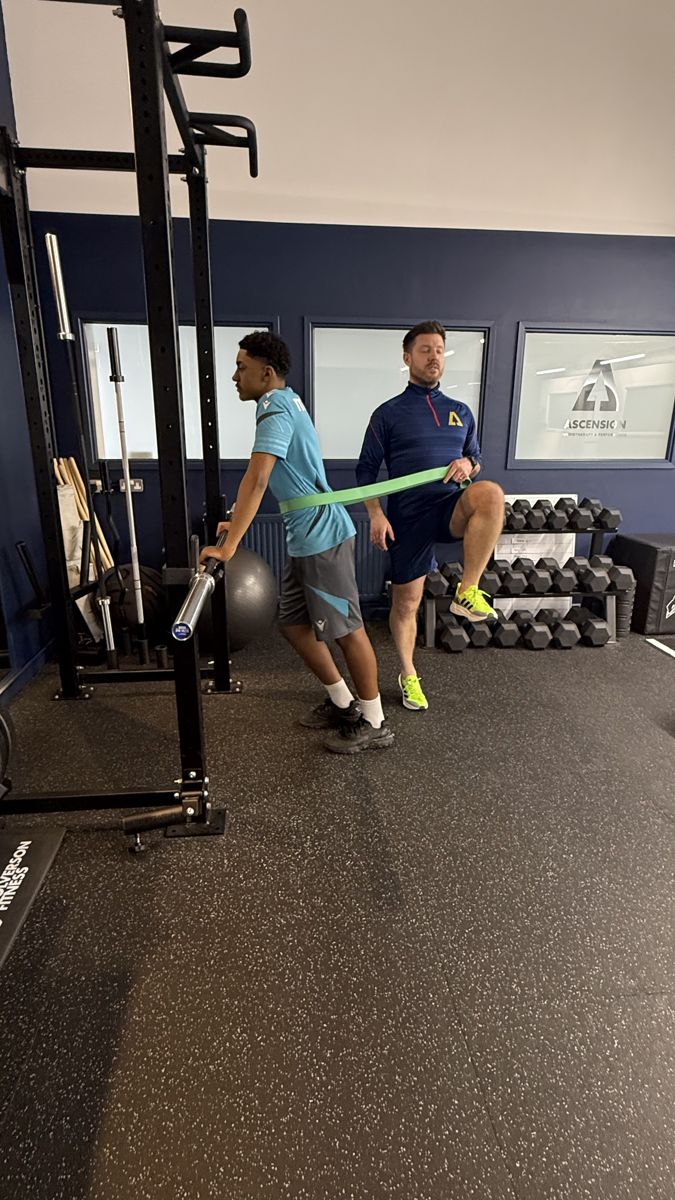 Coach supervising a young athlete's resistance band exercise at Ascension Physiotherapy & Performance